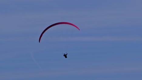 Bottom-view-of-paraglider-with-red-parachute-flying-circes-on-a-bright-blue-sunny-day
