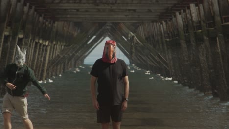 Two-masked-people-dance-under-the-legs-of-a-pier