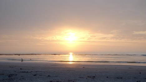 Sonnenaufgang-An-Einem-Bewölkten-Tag-Am-Strand,-Menschen,-Die-Am-Frühen-Morgen-Schwimmen