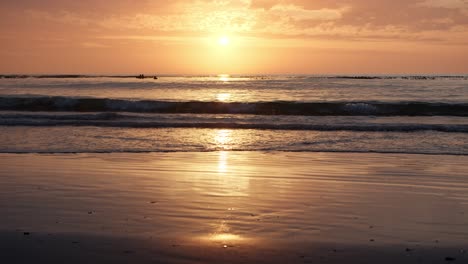 Der-Goldene-Sonnenaufgang-Spiegelt-Sich-Am-Sandstrand-Wider,-Während-Sich-Die-Wellen-Kräuseln