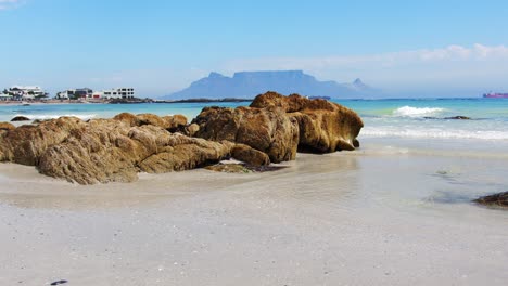 Slow-pan-across-the-white-sand-beach-and-rocks,-with-table-mountain-Cape-town-in-background