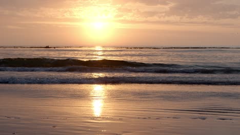 Der-Goldene-Sonnenaufgang-Spiegelt-Sich-Auf-Dem-Nassen-Strand-Wider,-Während-Die-Wellen-Brechen-Und-Sanft-Ans-Ufer-Spülen