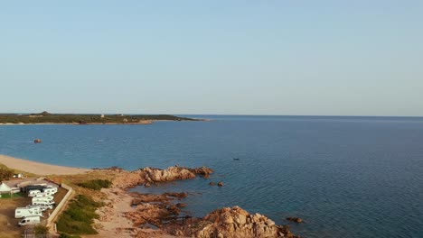 Tranquil-coast-of-Sardinia-with-camping-site-close-to-rocky-shore-aerial-forward