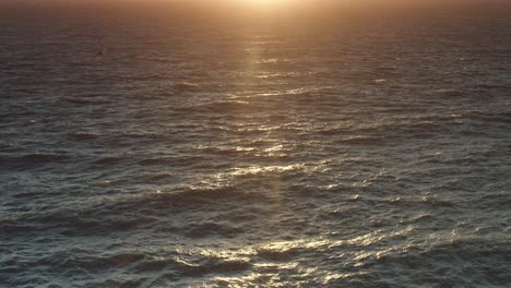 Ein-Tief-Stehender-Sonnenuntergang-Spiegelt-Sich-Auf-Einer-Aufgewühlten-See-Wider