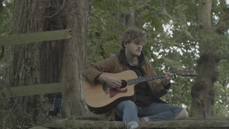 Caucasian-Male-Musician-Playing---Strumming-Guitar-in-Woods,-Static