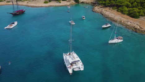 Revealing-drone-shot-of-moored-catamaran-and-people-diving-into-the-sea-near-bay