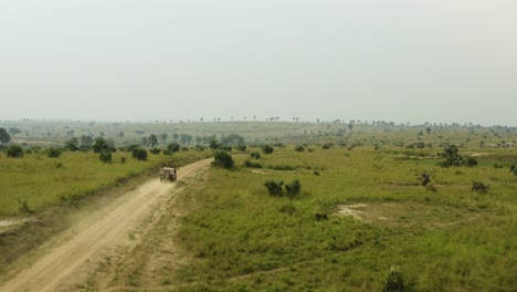 Car-speeds-along-dirt-road-to-destination-through-African-wilderness-with-green-vegetation