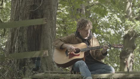 Young-man-plays-acoustic-guitar-and-sings-sitting-under-shady-tree