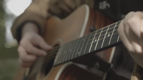 Hands-play-acoustic-guitar-with-soft-focus-outdoor-background,-Handheld-Closeup