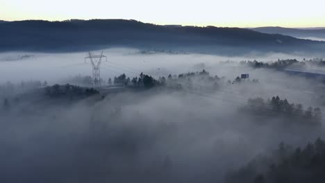 Aerial-view-of-a-misty-forest-with-big-electricity-towers-over-the-fog