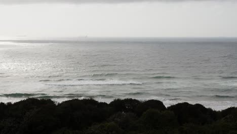 A-long-shot-of-waves-coming-onto-a-dark-beach-with-a-ship-just-barely-visible-in-the-distance