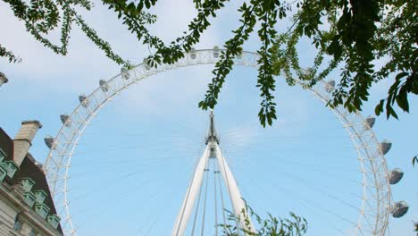 Slow-motion-gimbal-walk-of-The-London-Eye-under-green-trees-from-Jubilee-Park