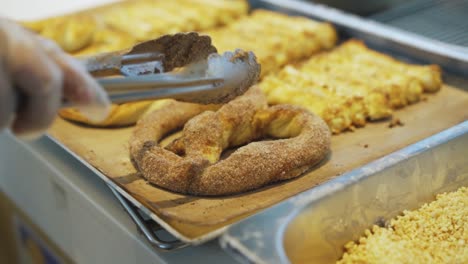 Person-Placing-Cinnamon-Sugar-Soft-Pretzel-On-A-Tray-With-Other-Freshly-Baked-Breads-In-Pastry-Kitchen---close-up,-slow-motion