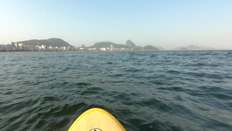 Stand-up-paddle-boarding-in-Rio-De-Janeiro-on-sea-by-beach-with-mountains-in-background