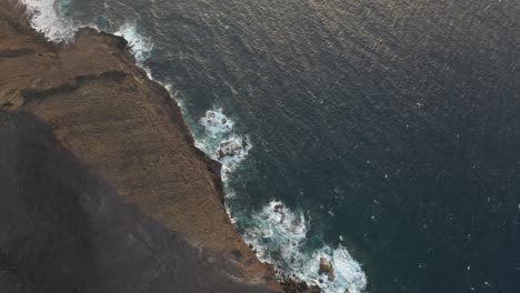 Relaxing-POV-aerial-shot,-high-above-dark-blue-ocean,-cliff-range,-tilt-up-to-horizon
