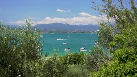 Breite-Aufnahme-Von-Booten-Im-See-Mit-Vorbeifahrendem-Jetski-Am-Jamaica-Beach,-Sirmione,-Lago-Garda,-Gardasee,-Italien