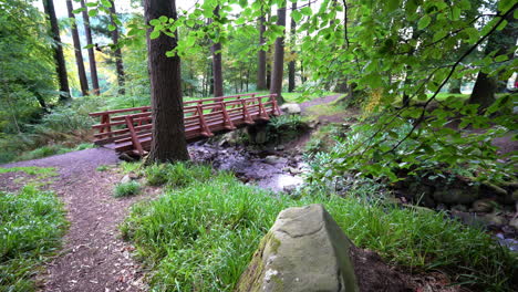Red-wooden-foot-bridge-over-a-fresh-water-creek--Ravensdale-Forest-Park,-Ireland