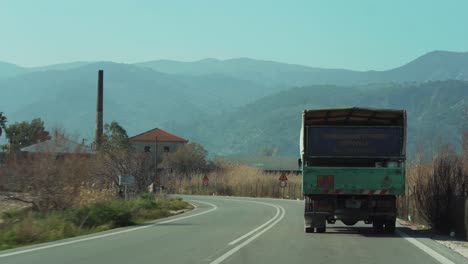 Truck-driving,-scenic-countryside-road,-entering-village,-POV-from-behind,-mountains