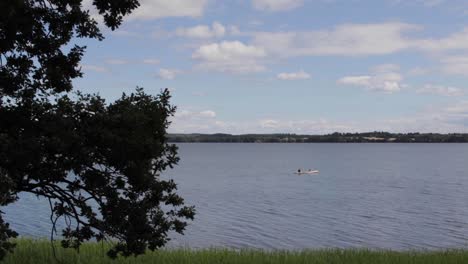 Glückliche-Menschen-Segeln-In-Kanus-Auf-Dem-Windigen-Wassersee-Mit-Wolken-Und-Bäumen-Im-Hintergrund