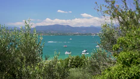Wide-establishing-shot-of-boats-in-the-lake-with-Jet-ski-passing-by,-on-Jamaica-Beach,-Sirmione,-Lago-Garda,-Lake-Garda,-Italy
