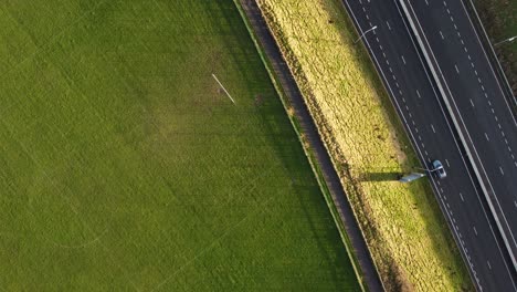 Static-overhead-aerial-drone-clip-of-a-football-field-meeting-a-highway-separated-by-a-path-in-Manchester,-UK