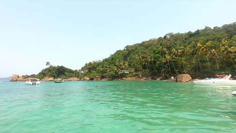 Isla-Tropical-Con-Agua-Azul-Verde-Y-Palmeras,-Barcos-Flotando-Frente-Al-Cielo-Azul-Y-Rocas-En-Isla-Grande-Brasil
