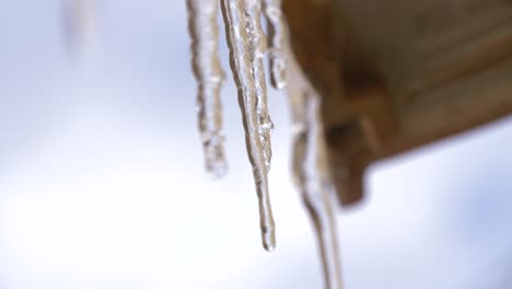 Icicles-hanging-from-a-roof-with-a-cloudy-blue-sky-in-the-background-dripping-water