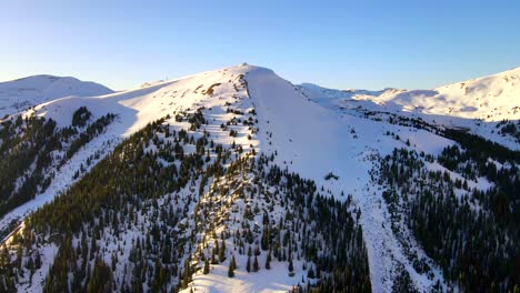 Tilt-up-drone-view-of-forest-clad-mountain-covered-in-snow