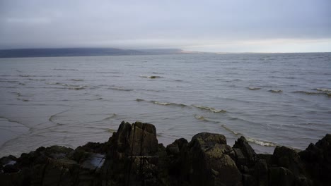 Blick-Auf-Den-Sandstrand-Und-Die-Wellen-Am-Meer,-Die-Felsige-Küste-Und-Den-Bewölkten-Himmel-In-Dundalk,-Irland
