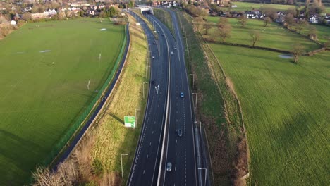 Static-aerial-drone-clip-of-a-highway-with-cars-passing-and-an-intersection-with-houses-and-a-dog-playing-in-background-in-Manchester,-UK