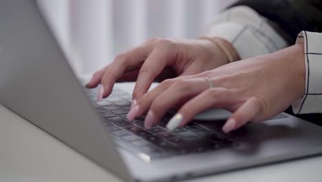 Close-up-shot-of-white-caucasian-female-hands-typing-on-a-laptop-while-sitting-at-office-desk-indoors