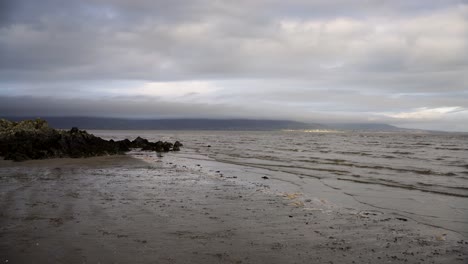 Mud-and-sand-on-the-beach,-sea-waves-and-rocky-coast-,-cloudy-sky-in-Dundalk,-Ireland