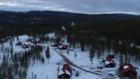 Slow-flight-over-a-snowy-village-in-a-little-valley-framed-by-trees-in-Fulufjallsbyn,-Sweden