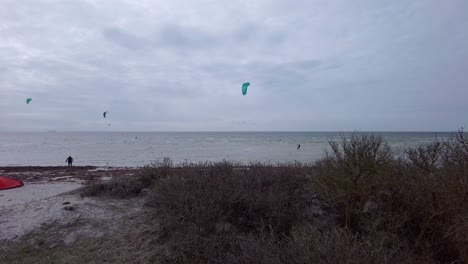 Total-view-of-three-kite-surfers-on-the-sea-riding-the-waves-under-windy-conditions,-view-from-distance