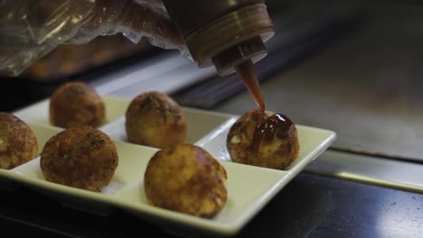 Chef-Putting-Sauce-In-Plated-Takoyaki-Balls