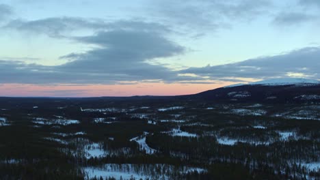 Smooth-drone-flight-over-the-snowy-landscape-of-sweden-with-a-light-red-glow-at-the-horizon-of-the-undergoing-sun