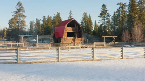 Sliding-shot-of-perfect-red-barn-sitting-in-a-snowy-farmland-field-at-sunrise