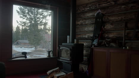 Interior-log-cabin-next-to-cold-fireplace-with-a-window-view-to-a-snowy-farm