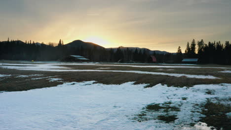 Luftfliege-über-Schneebedecktes-Ackerlandfeld-Und-Ranch-Bei-Sonnenuntergang