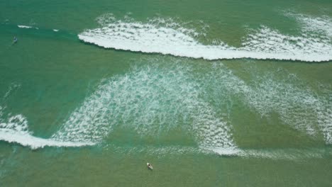 Drone-shot-flying-over-surfers-in-clear-water---Tofo,-Mozambique