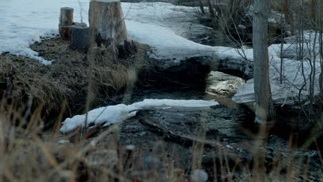 Pan-up-flowing-creek-revealing-frozen-farm-at-sunrise