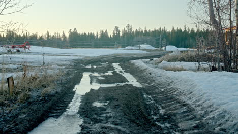 Frozen-muddy-dirt-road-leading-to-farm-entrance-at-sunrise