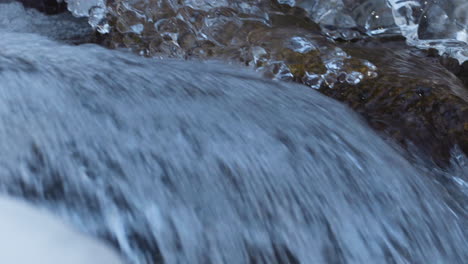 Detail-shot-of-river-water-flowing-during-winter-with-icicles-on-the-side,-pan-right