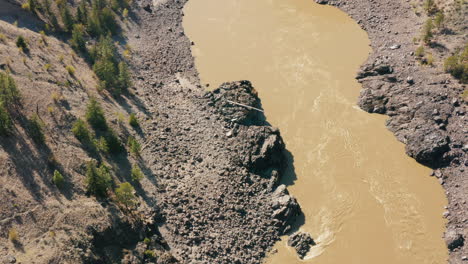 Aerial-birds-eye-of-brown-river-flowing-through-rocky-valley-gorge