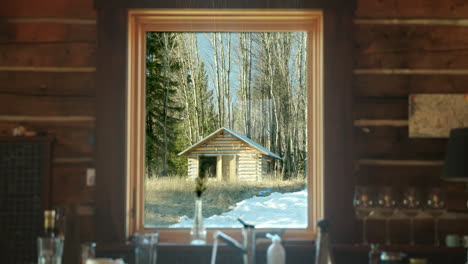 Interior-log-cabin-window-view-of-another-small-cabin-at-sunrise
