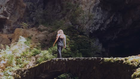Woman-Walking-Over-A-Natural-Bridge,-Rocky-Cave-Landscape---wide-shot