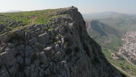 Aerial-view-revealing-a-person-on-top-of-Mount-Arbel,-in-sunny-Israel---tilt,-drone-shot