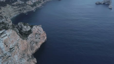 AERIAL---The-rocky-Mediterranean-cliffs-of-Ibiza,-Spain,-wide-spinning-shot