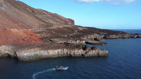 Cala-Tacoron-Bay,-which-is-traveled-by-a-speedboat-with-a-group-of-people-around-the-rocky-coast-on-a-calm-sea-on-a-sunny-day,-El-Hierro---aerial-shot