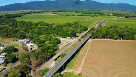 Aerial-View-Of-Road-Bridge-Through-Fields-And-Near-Mountain-Landscape-In-Cairns,-Queensland,-Australia